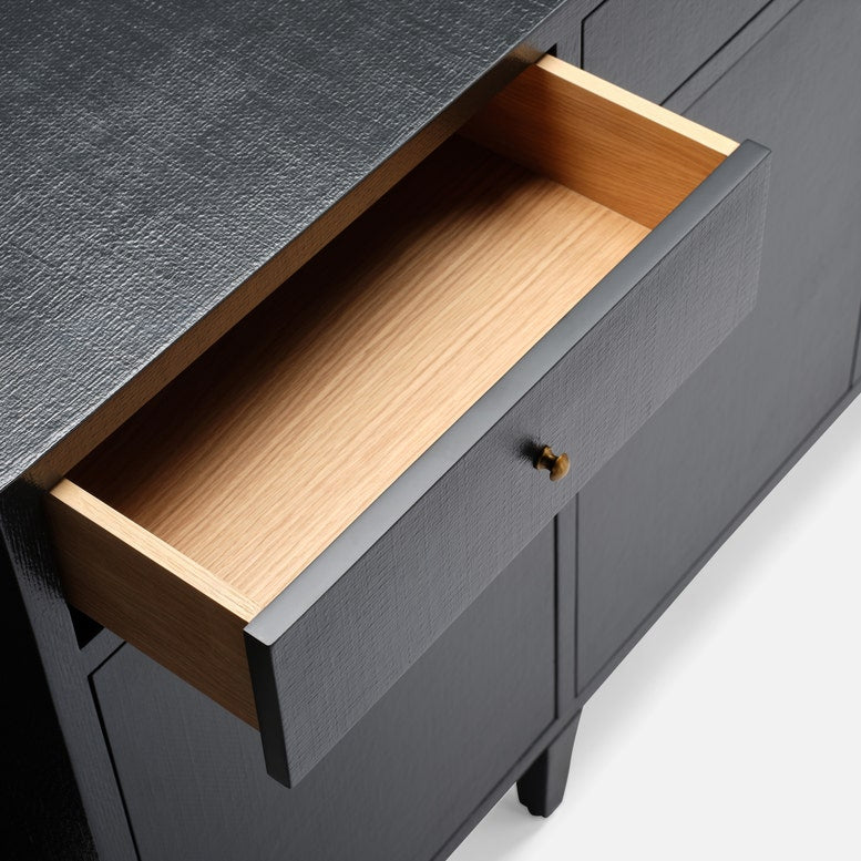 Close-up of a dark charcoal gray wooden cabinet with a textured finish, featuring an open drawer that reveals a light natural wood interior and a small brass pull handle.