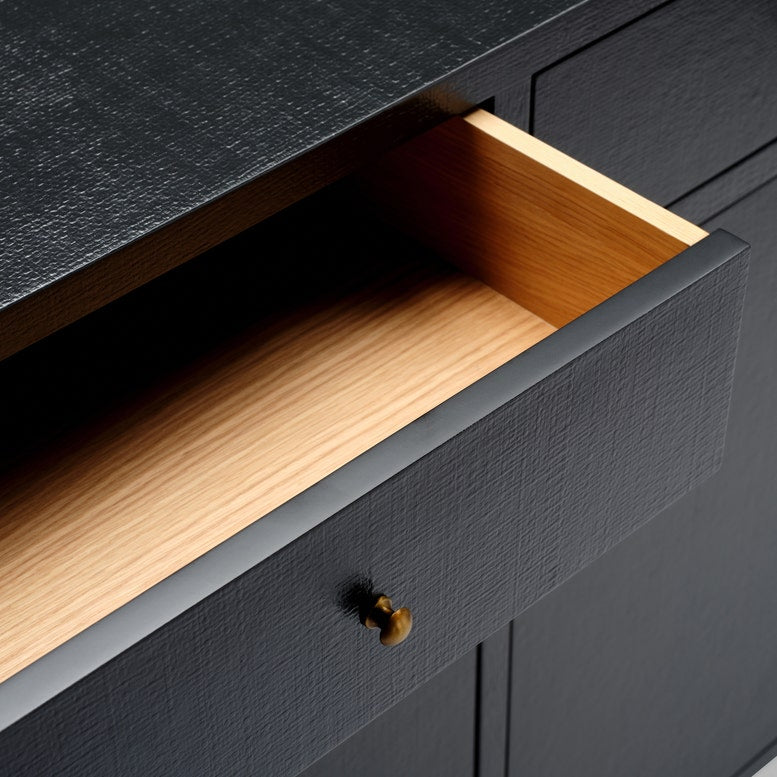 Close-up of a dark charcoal textured drawer with a light natural wood interior and a small brass pull handle.