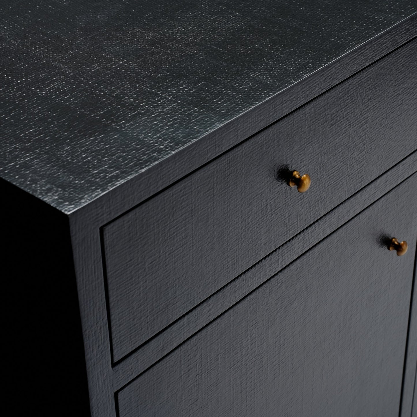 Close-up of a dark charcoal textured cabinet with two drawers and two small round metallic knobs, shown against a black background.