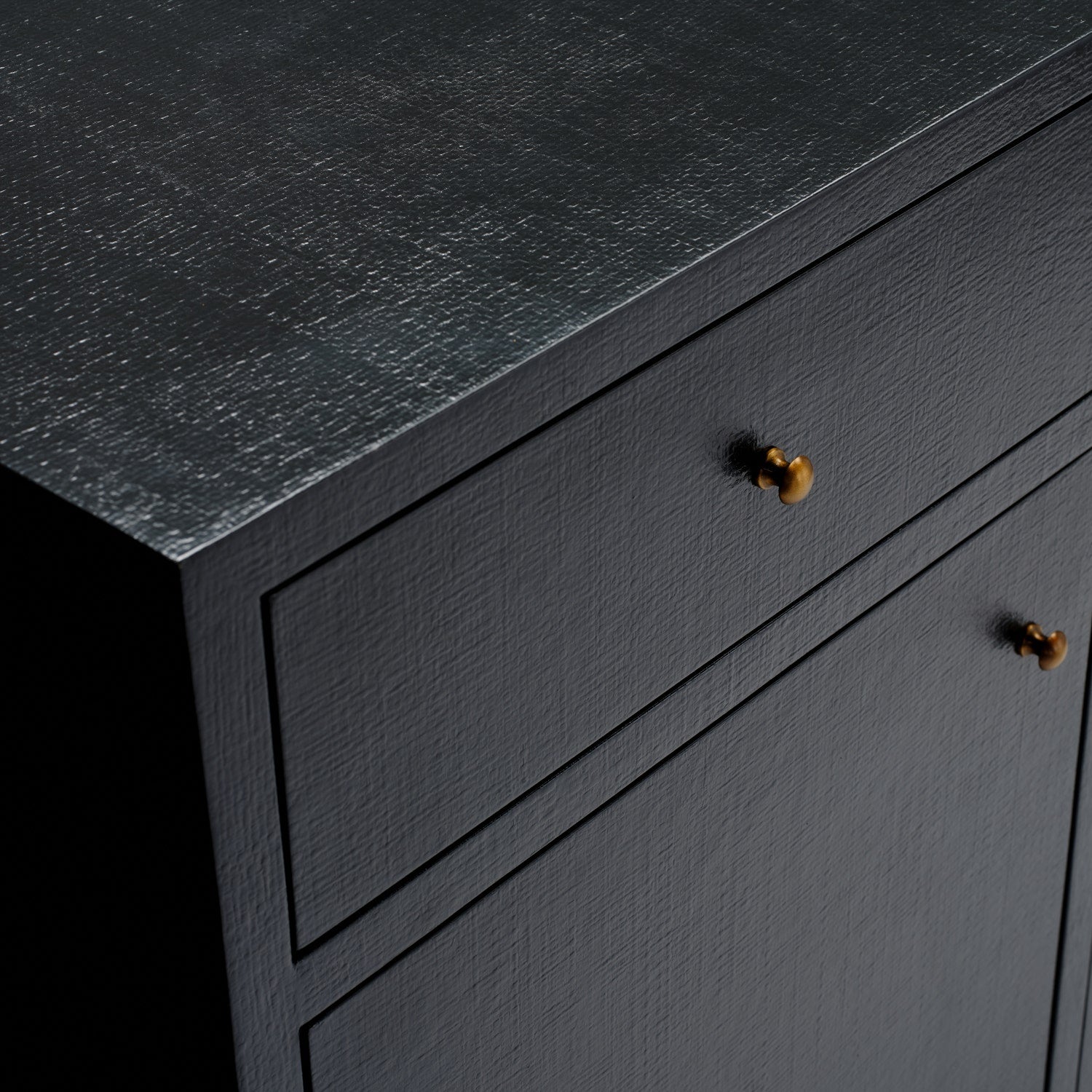 Close-up of a dark charcoal textured cabinet with two drawers and two small round metallic knobs, shown against a black background.