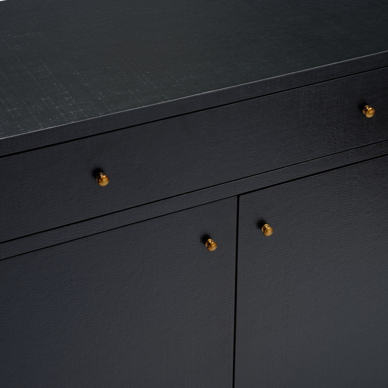 Close-up of a black wooden cabinet with a textured finish and small round gold-toned drawer pulls, showing part of the top surface and front doors.
