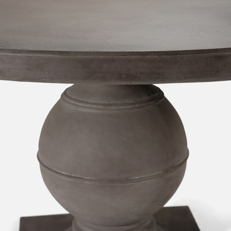 A close-up of a round dining table featuring a dark gray wood top and a matching round pedestal base with a matte finish, set against a plain white background.