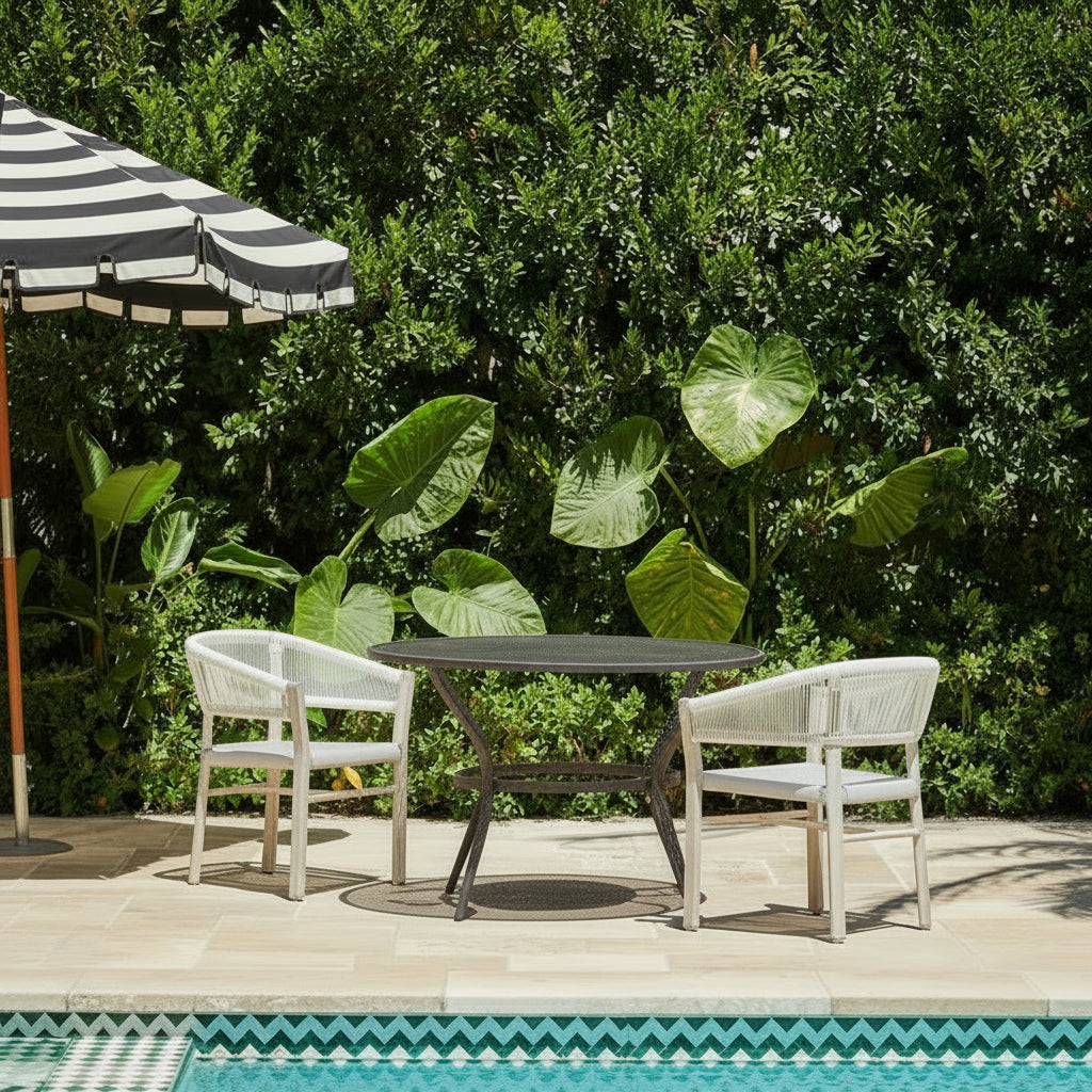 Outdoor patio set with table and chairs by a pool, surrounded by greenery.