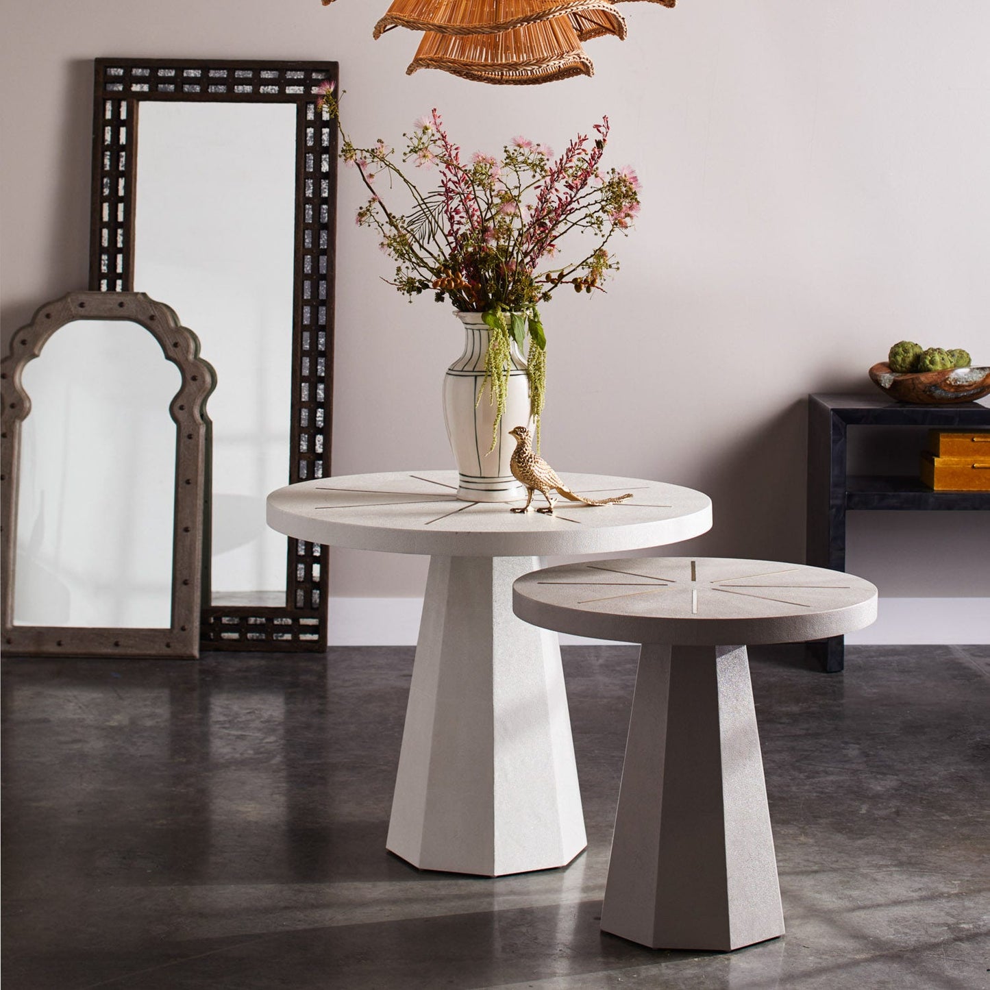Two round marble tables with a vase of flowers and decorative items in a room with mirrors and a small table.
