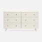 An off-white double dresser with six drawers, featuring small round brass pull knobs and tapered legs, shown against a light gray background.
