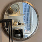 Round decorative mirror with metallic frame on a wall, reflecting a room interior.