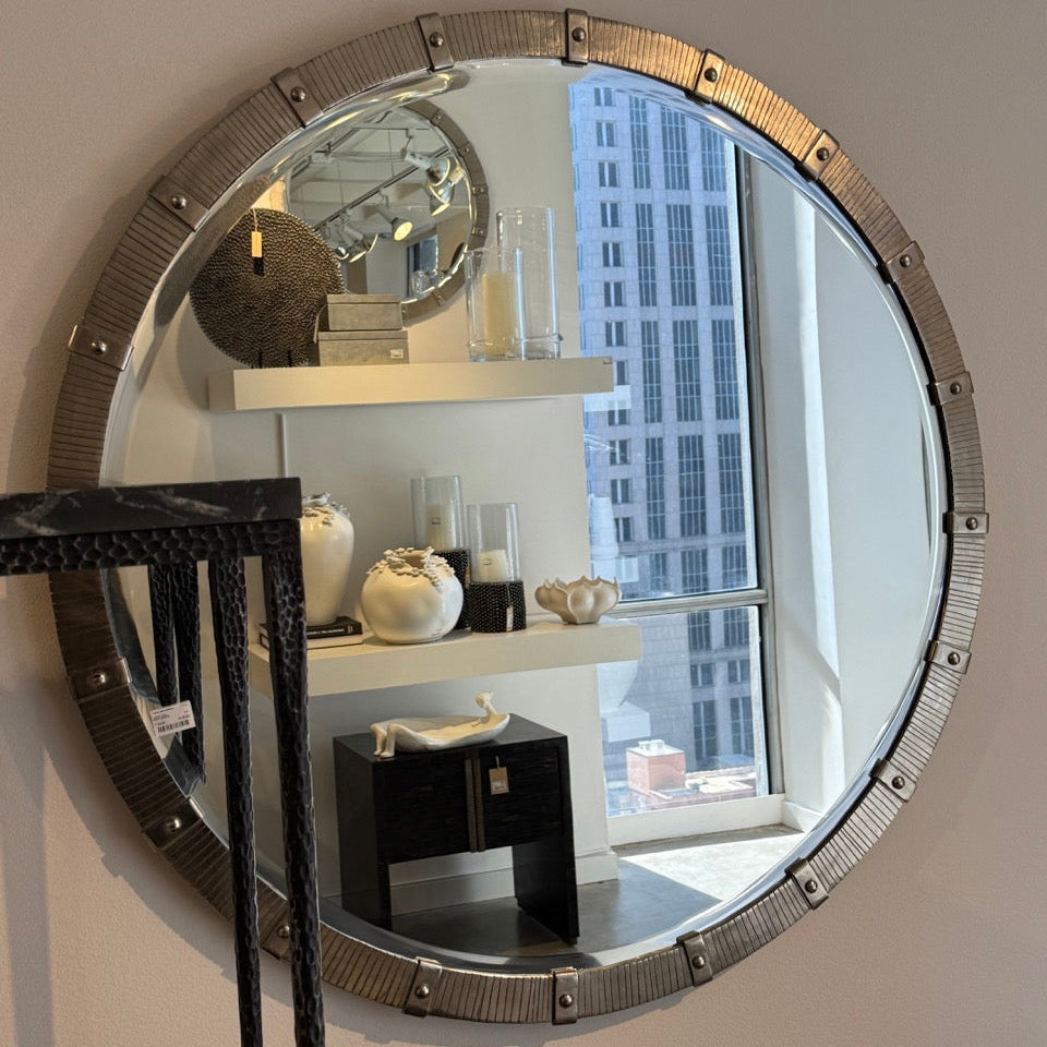 Round decorative mirror with metallic frame on a wall, reflecting a room interior.