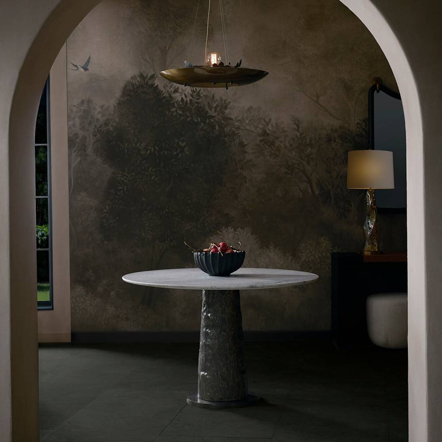 Round marble table with a bowl of fruit against a textured wall in a dimly lit room.