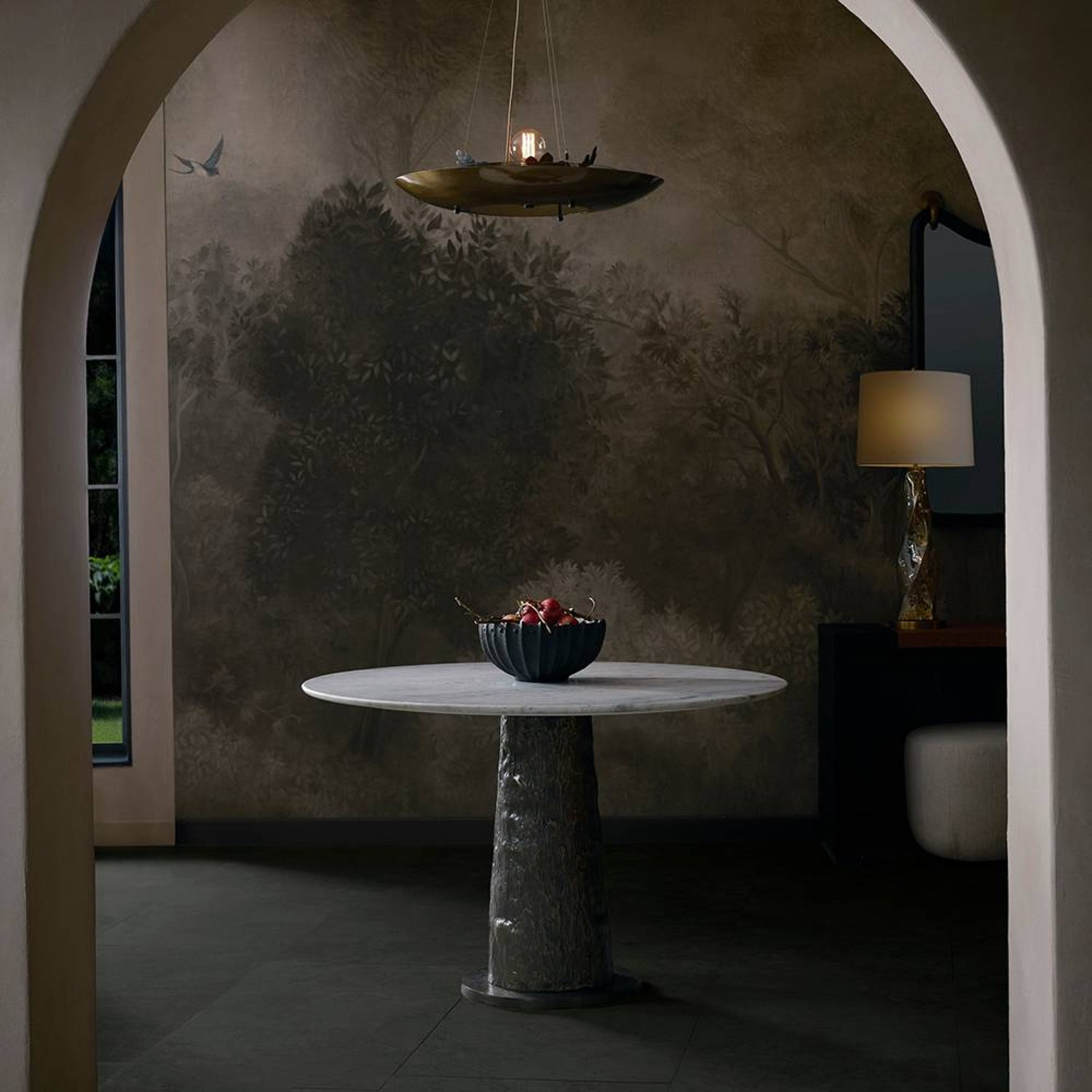 Round marble table with a bowl of fruit against a textured wall in a dimly lit room.