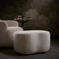 Beige armchair and ottoman with a small round table in a dimly lit room.