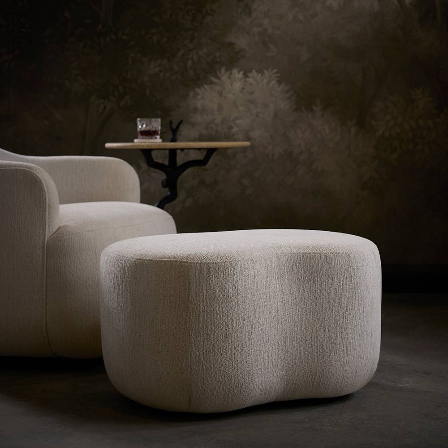 Beige armchair and ottoman with a small round table in a dimly lit room.