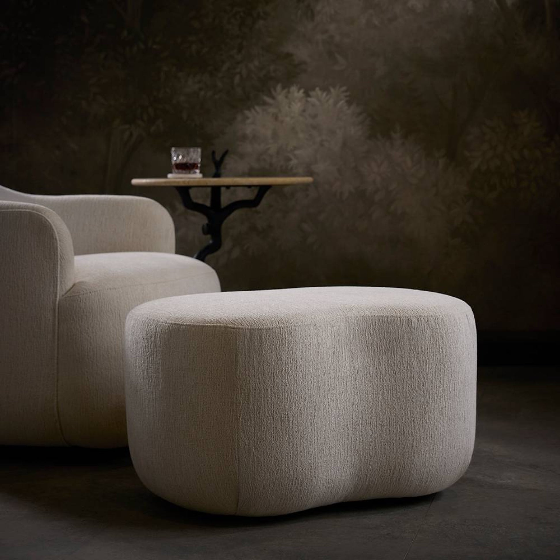 Beige armchair and ottoman with a small round table in a dimly lit room.