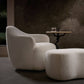 Modern beige armchair and ottoman with a small round table in a dimly lit room.