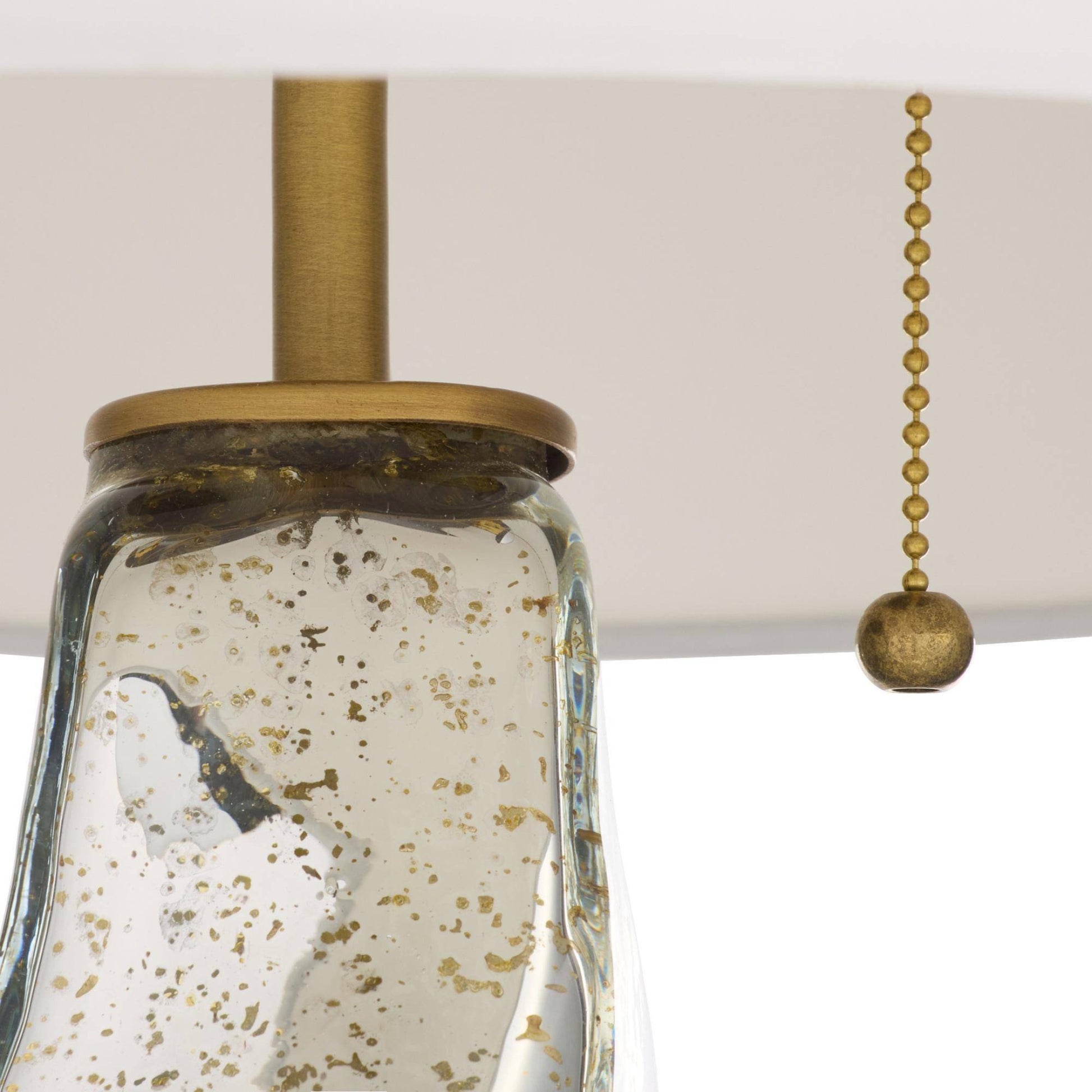 Close-up of a pendant light fixture with glass shade and brass pull chain.