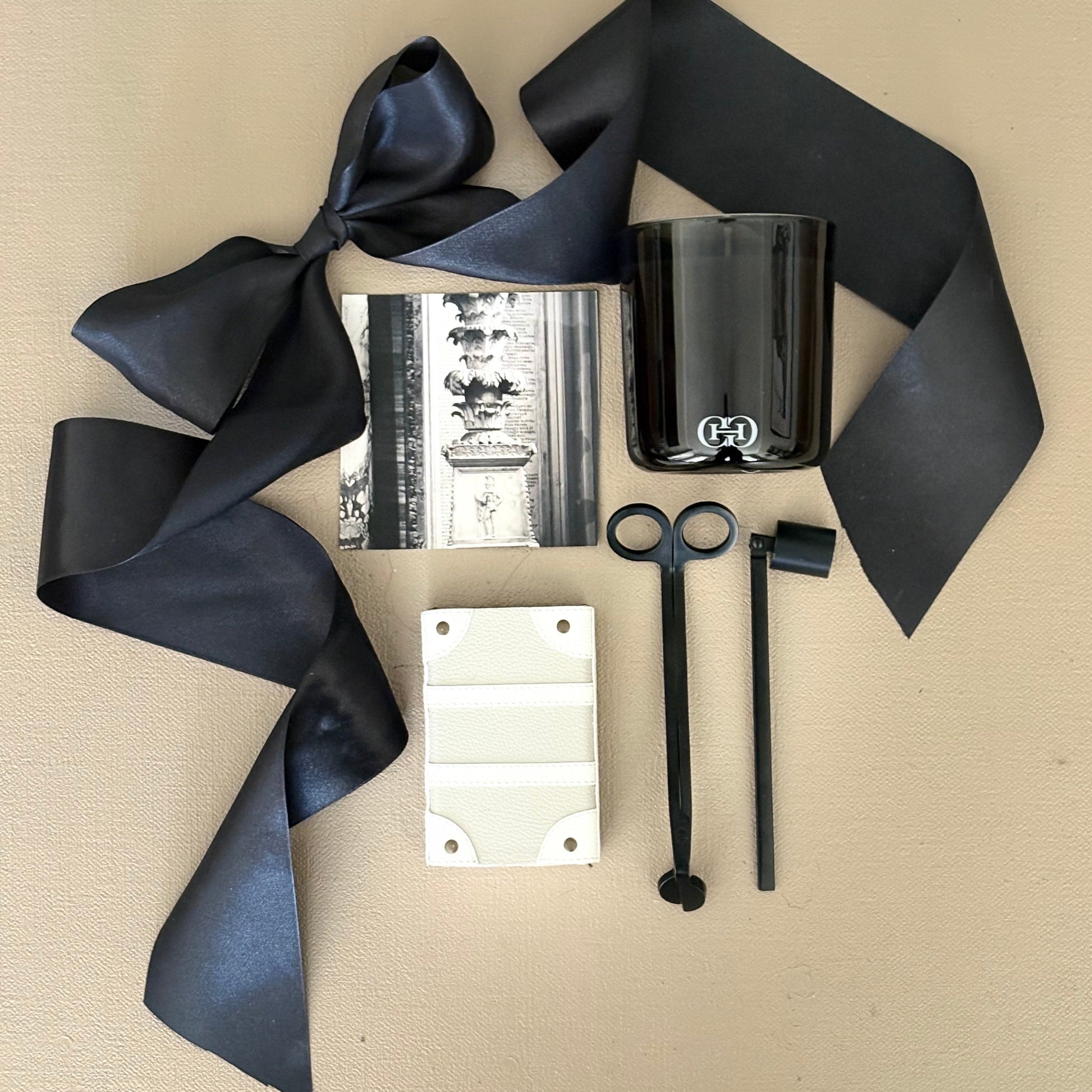 Black ribbon, black candle, black scissors, black straws, and white card on a beige surface
