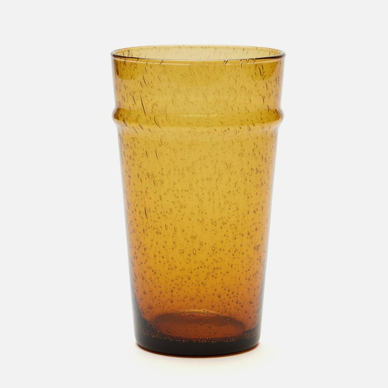 An amber-colored translucent glass tumbler with a speckled texture and a flared rim, shown against a plain white background.