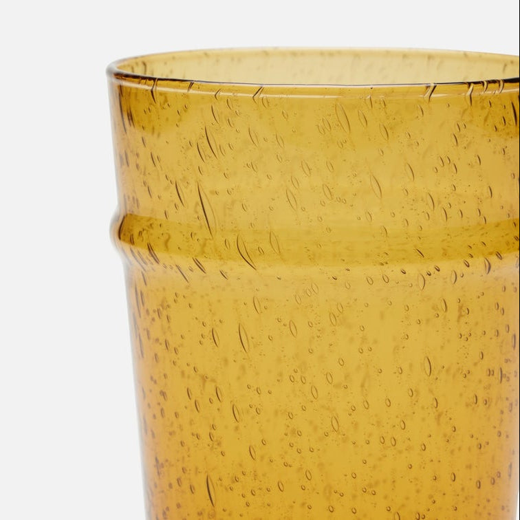 Close-up of a translucent amber glass cup with a textured, bubbly finish on a plain white background.