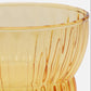 Close-up of a translucent amber glass bowl with vertical ribbed texture and a flared base, shown against a light neutral background.