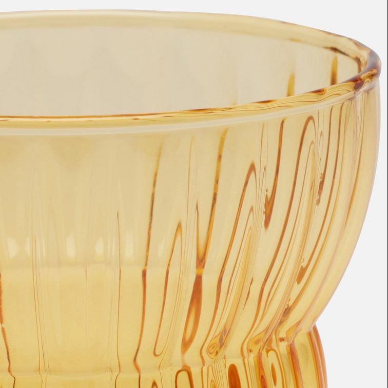 Close-up of a translucent amber glass bowl with vertical ribbed texture and a flared base, shown against a light neutral background.