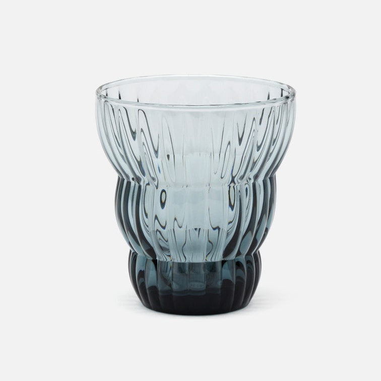 A ribbed, fluted glass tumbler with a gradient color transition from light blue-gray at the top to a deep black at the base, shown on a clean white background.