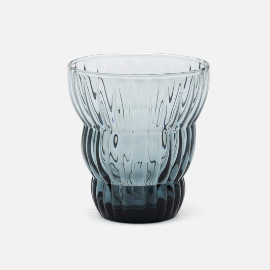 A ribbed, fluted glass tumbler with a gradient color transition from light blue-gray at the top to a deep black at the base, shown on a clean white background.
