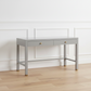 Gray desk with two drawers on a wooden floor against a white wall