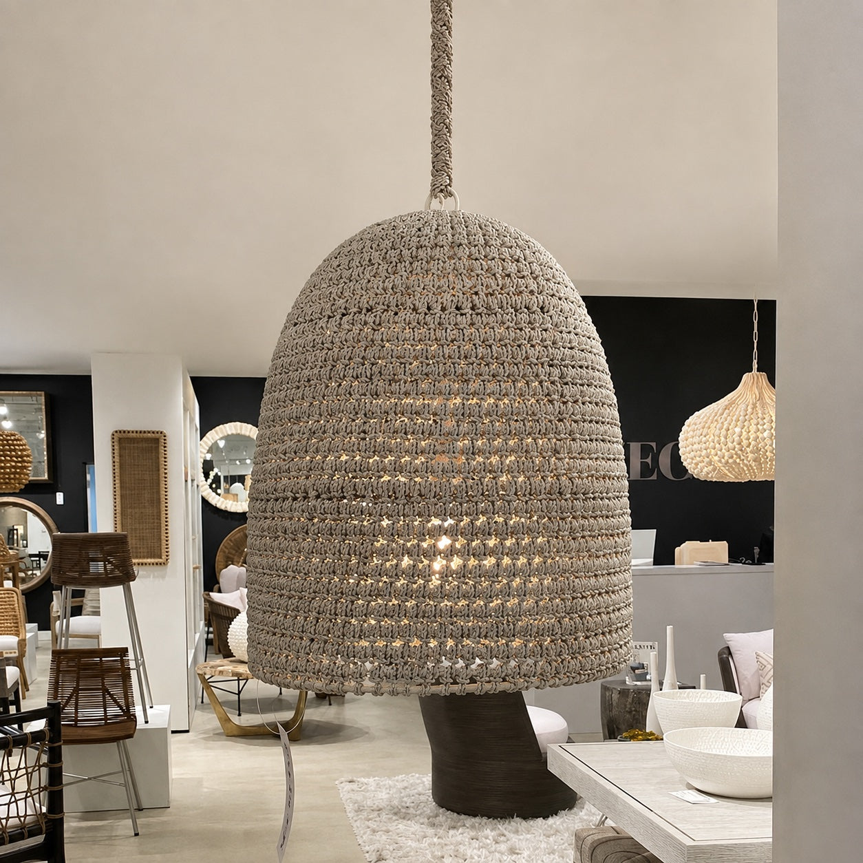 A large woven pendant light in a natural beige tone hangs in a modern, stylishly decorated interior showroom.