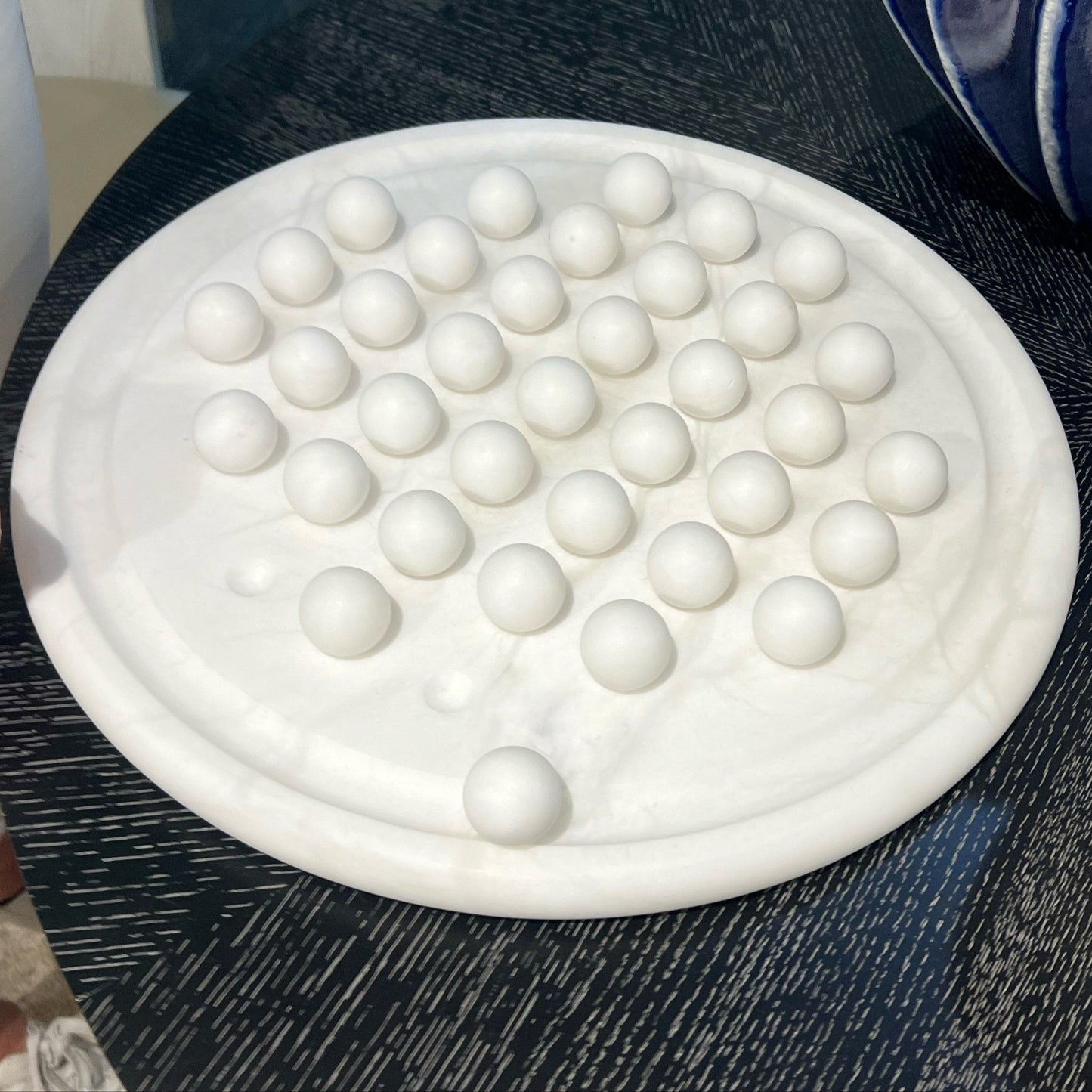 White spherical object on a textured surface with a person and blue and white striped object in the background.