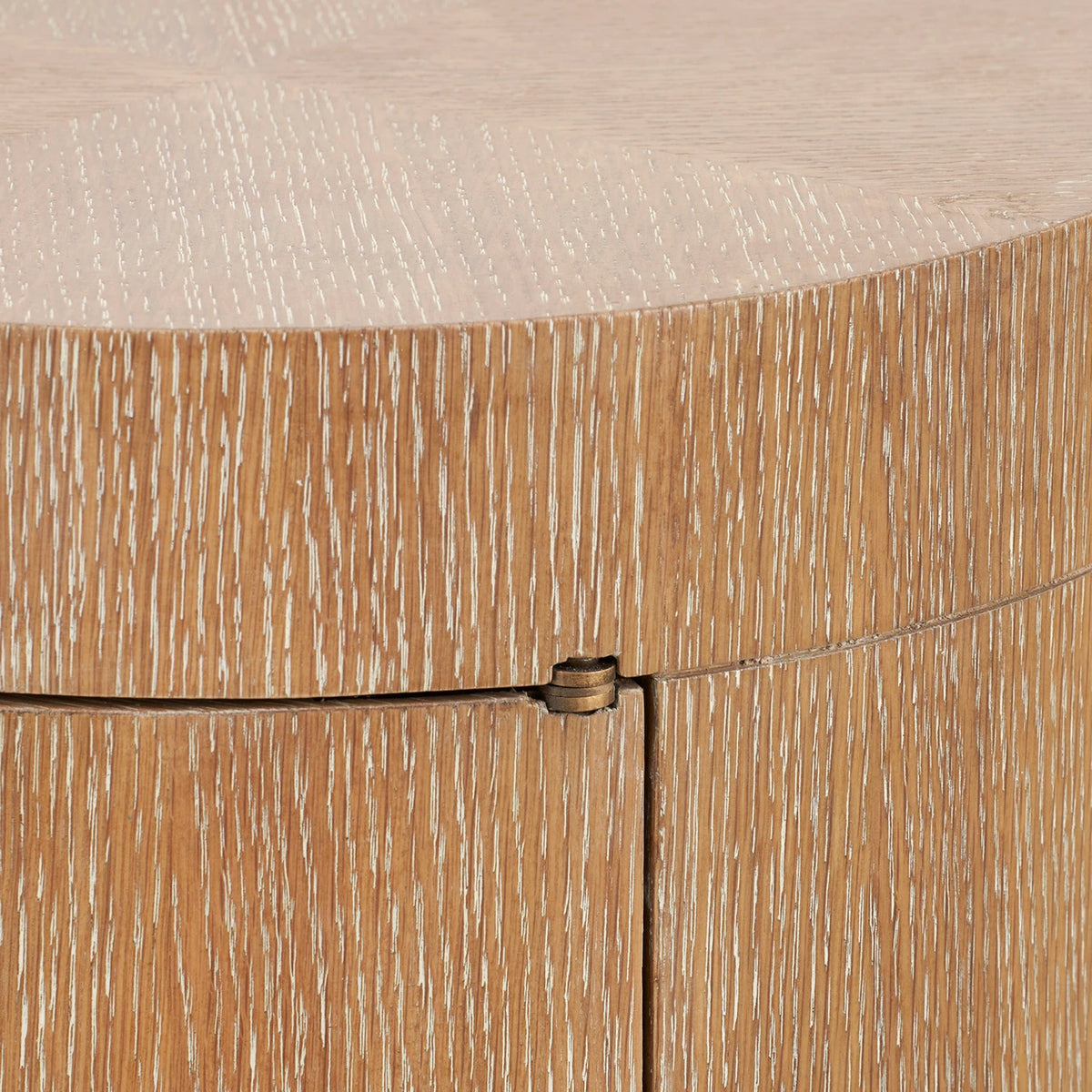Close-up detail of a light oak wood cabinet showing the grain texture, a small brass pull handle, and the seam between the front doors.