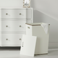 White laundry basket with wooden top in front of a white dresser.