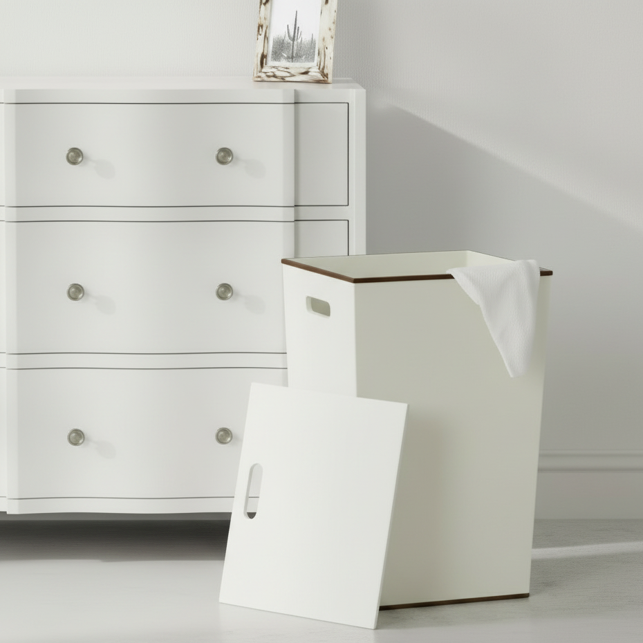 White laundry basket with wooden top in front of a white dresser.