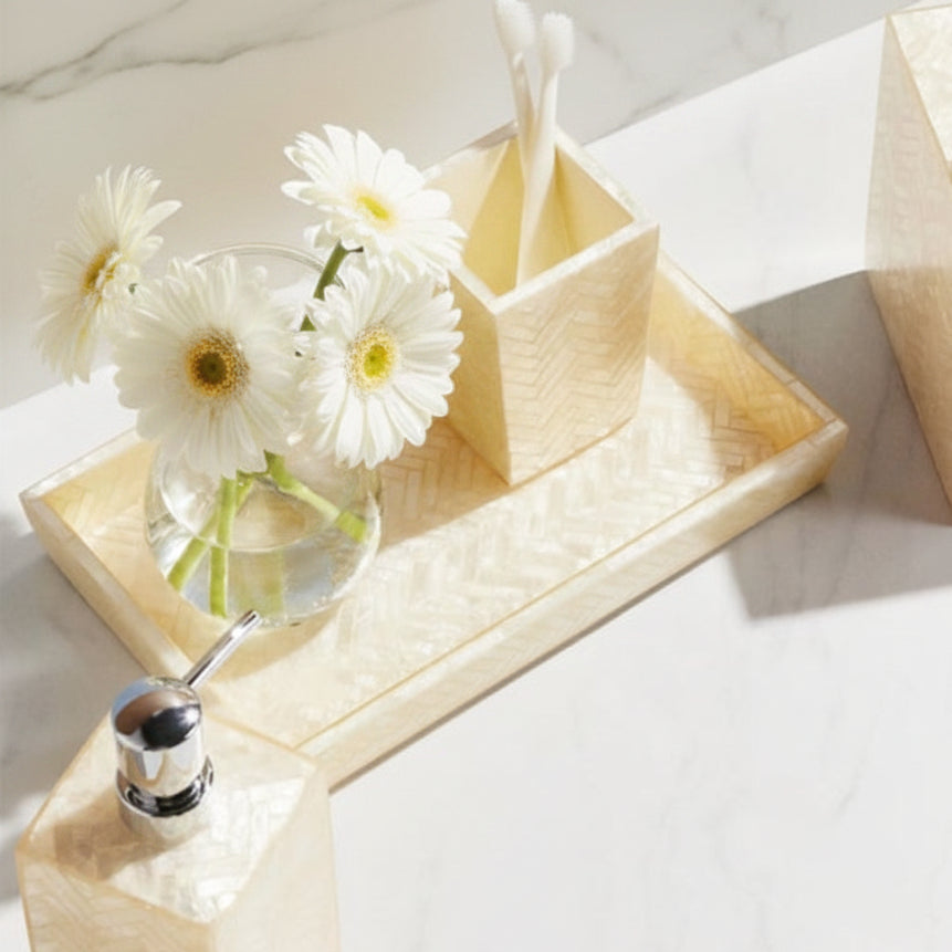 A coordinated bathroom accessory set in a light cream herringbone pattern, including a tissue box cover, soap dispenser, tray, and tooth holder, styled with flowers on a white marble surface.