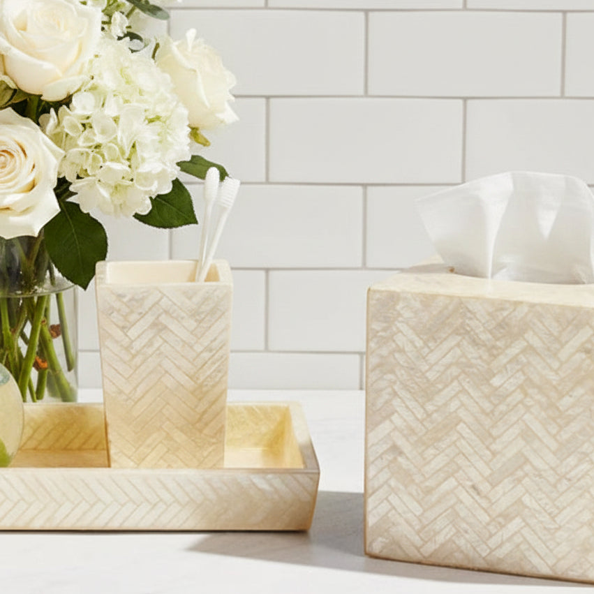 A bathroom tissue box cover and matching toothbrush holder set in a light beige herringbone pattern, styled on a white countertop against a light subway tile backsplash.