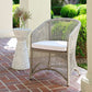 Wicker chair with a white cushion on a patio with a small table and plants.