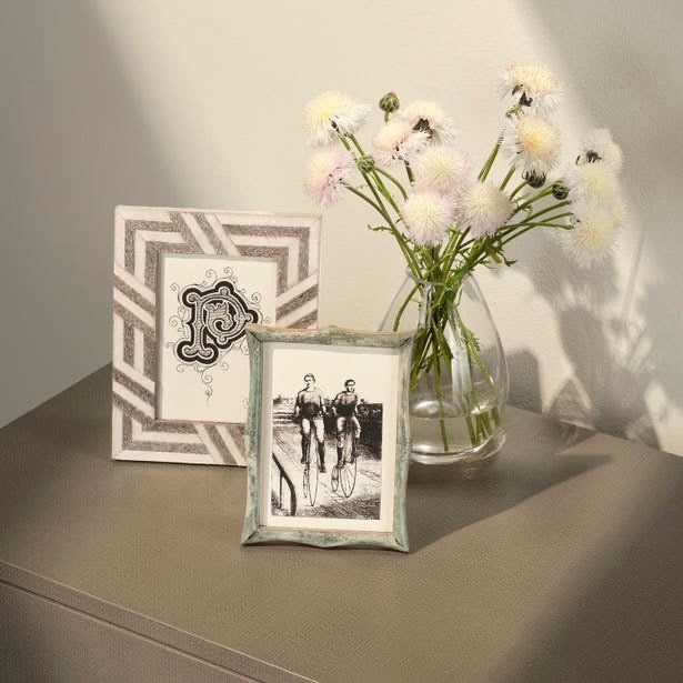 Two framed pictures and a vase with flowers on a surface.