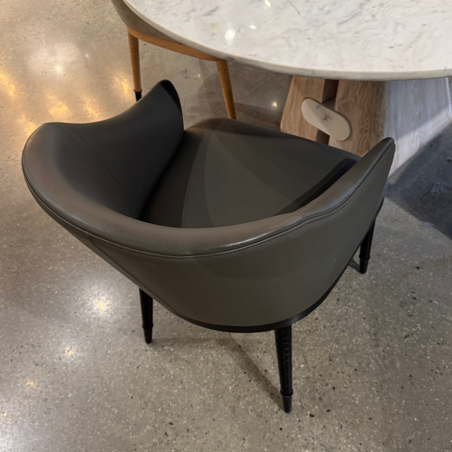 Modern dark gray chair in a showroom setting with a marble table in the background.