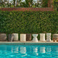 Decorative outdoor stools by a pool with greenery in the background