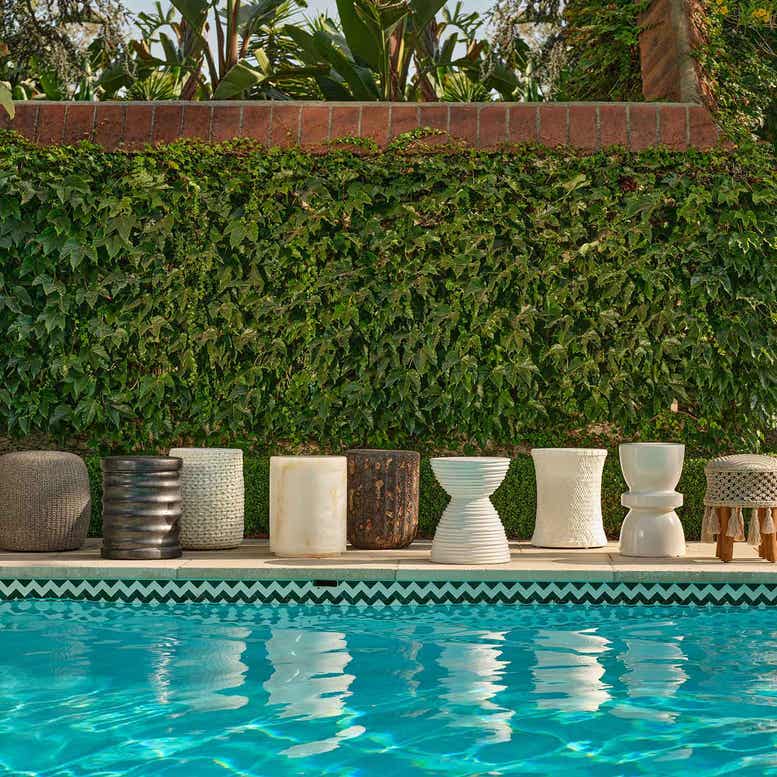 Decorative outdoor stools by a pool with greenery in the background