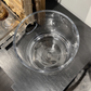 Clear glass bowl on a dark surface with a decorative frame in the background