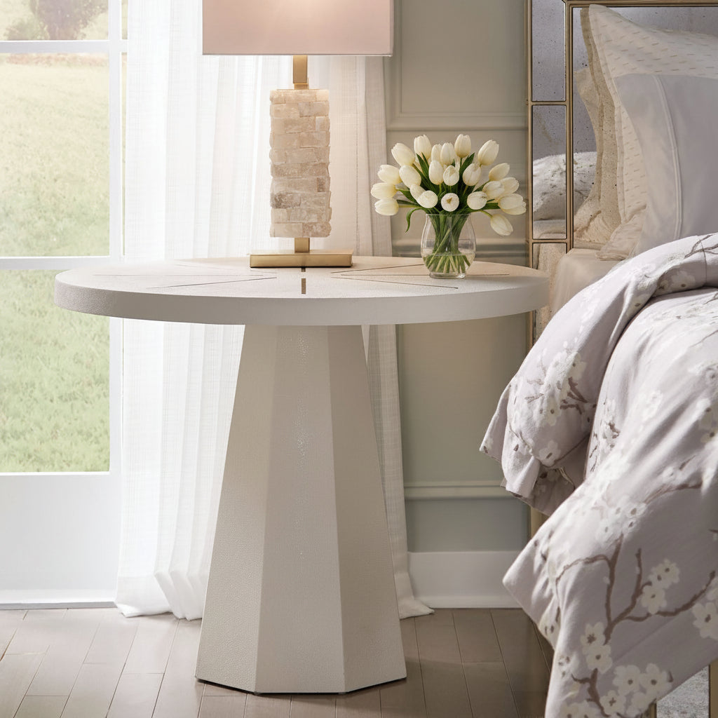 Round white table with a lamp and flowers in a bedroom setting