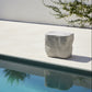 Modern outdoor chair by a pool with a white wall and greenery in the background