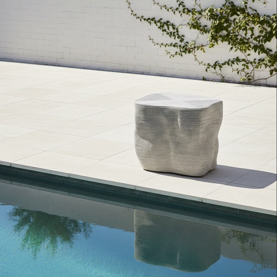 Modern outdoor chair by a pool with a white wall and greenery in the background