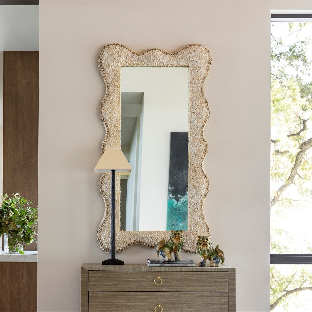 Wooden dresser with decorative mirror and lamp in a room with a window and bench.