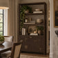 A tall dark brown rattan cabinet with open shelves and two lower cabinet doors, styled with books, bowls, bottles, and potted plants in a warm dining room setting.