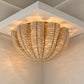 A woven natural-fiber flush-mount ceiling light fixture with a scalloped shell-like form, shown illuminated in a warm light reflecting on a white ceiling and wall.
