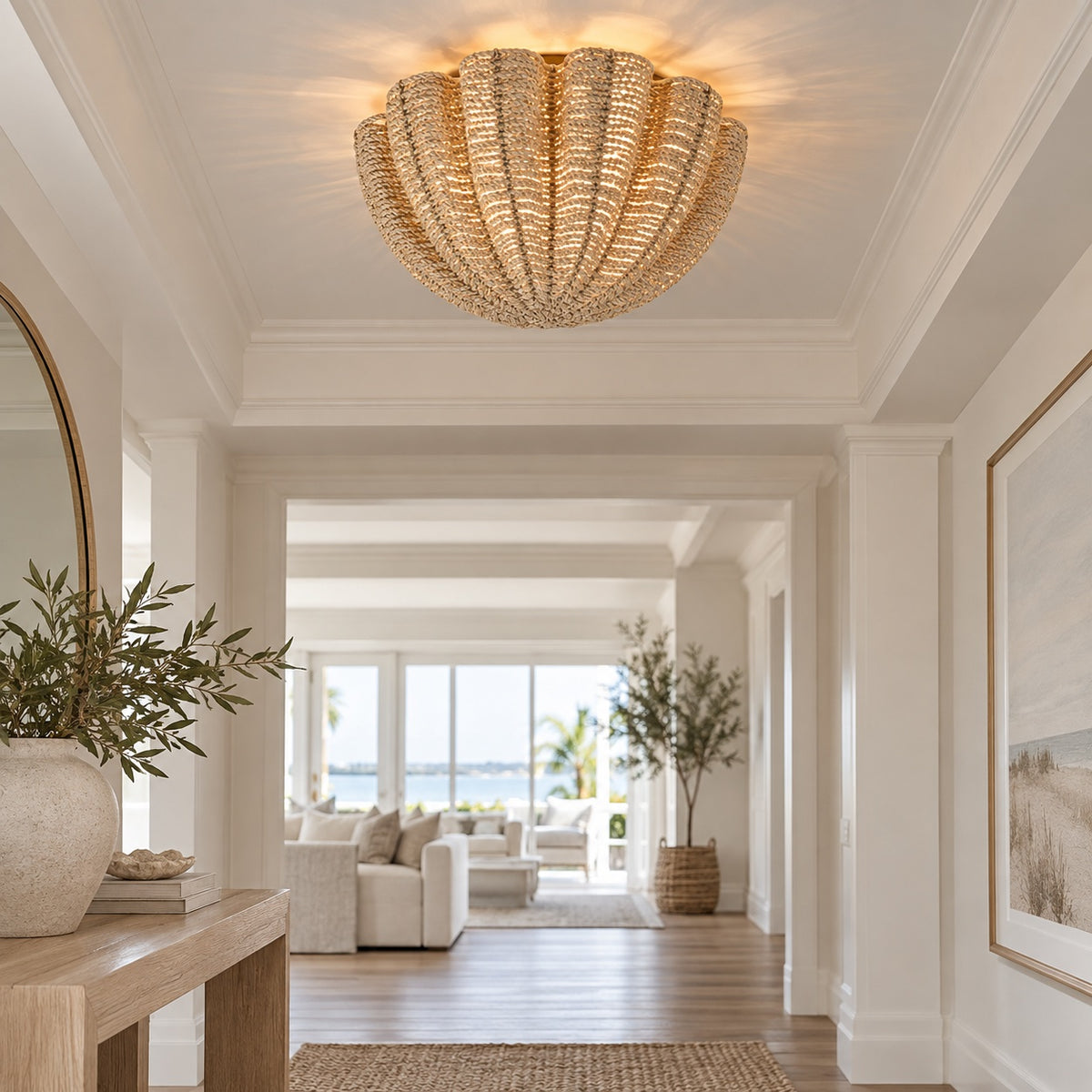 A glowing woven ceiling light fixture in a bright, modern hallway with white walls, wood floors, and a view of a beachfront living room in the distance.