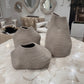 Three textured woven vases in a neutral taupe-beige color arranged on a white marbled table inside a modern living room showroom.