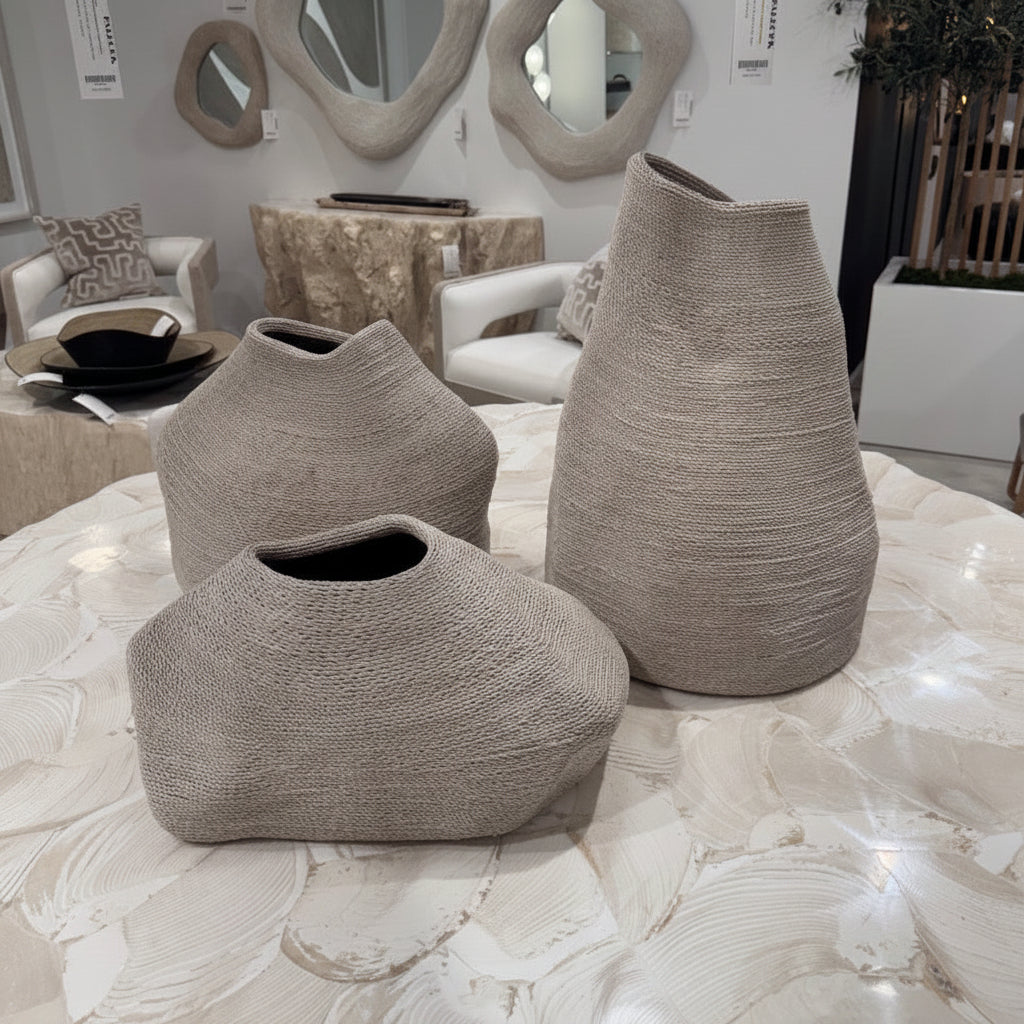 Three textured woven vases in a neutral taupe-beige color arranged on a white marbled table inside a modern living room showroom.