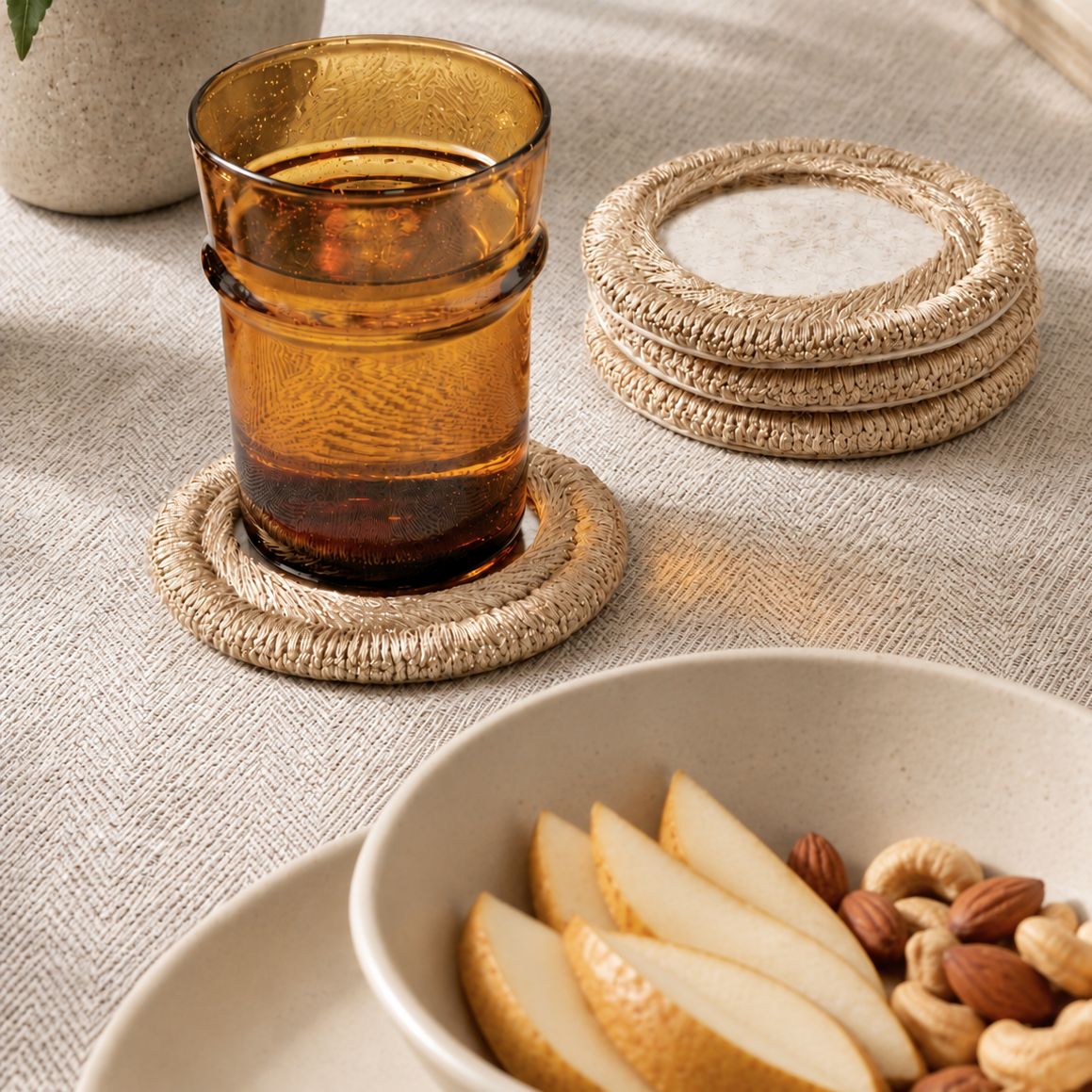 Amber glass tumbler resting on a woven round coaster, with a stack of matching woven coasters and a beige textured tabletop in the background.