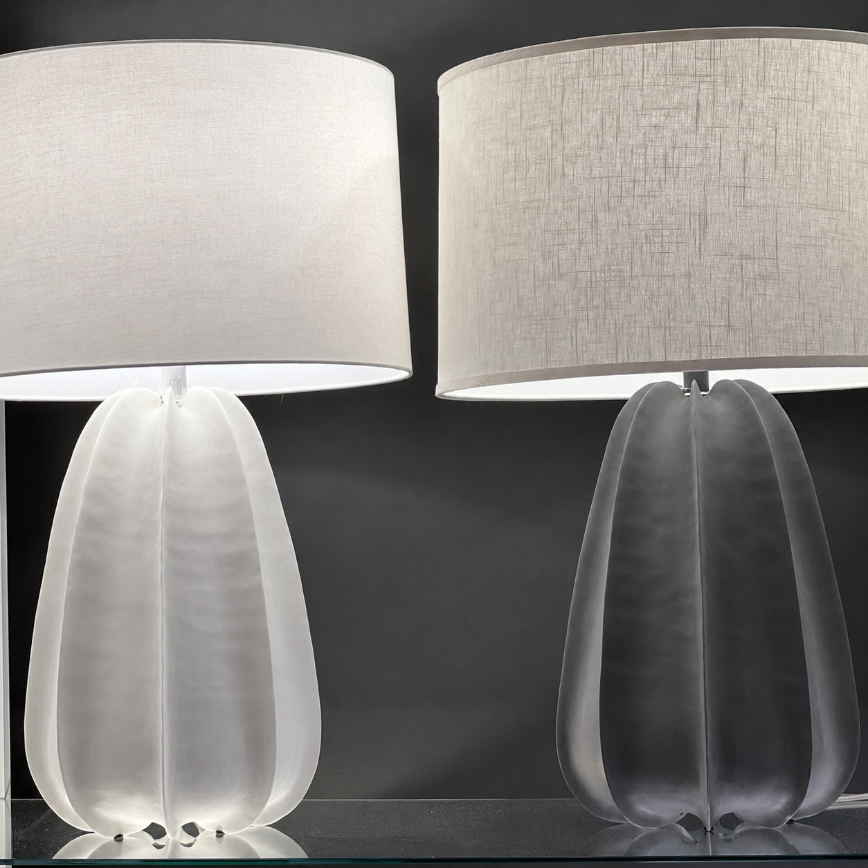 Two modern table lamps with textured drum shades and sculptural tulip-shaped bases, shown side by side against a dark gray background.